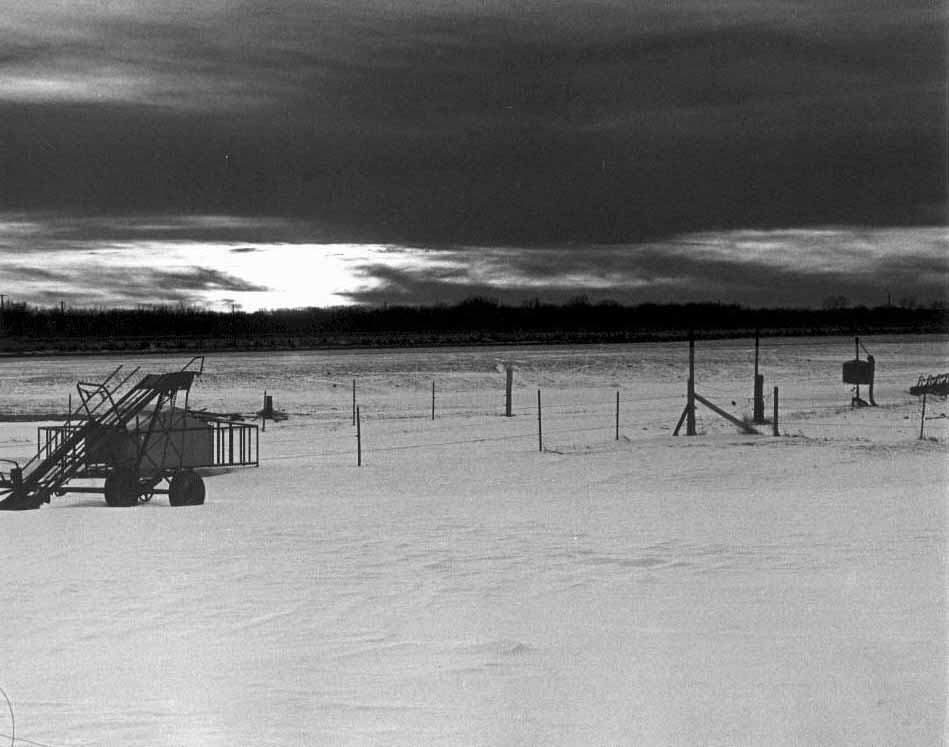 Sun setting on Iowa snow and farmland with deserted equipment in foreground.